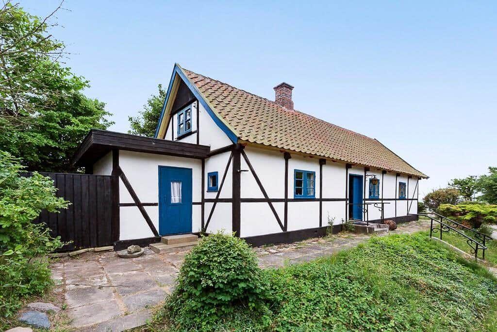 Ein weißes Fachwerkhaus mit blauen Fenstern und Tür unter einem Ziegeldach.