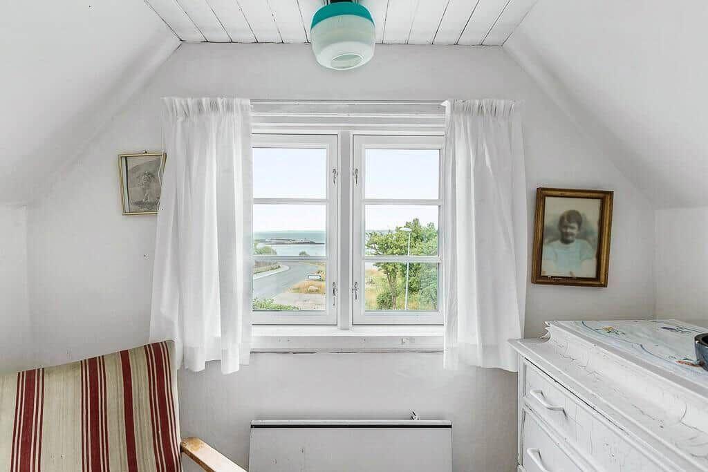 Schlafzimmer mit Dachfenster, Blick aufs Meer, weiße Wände und Vorhänge.