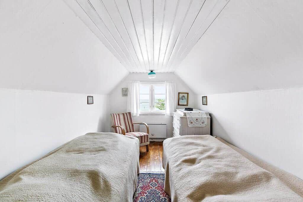 Zwei Betten unter einem Dachboden, ein Fenster, ein Stuhl und ein Schrank.