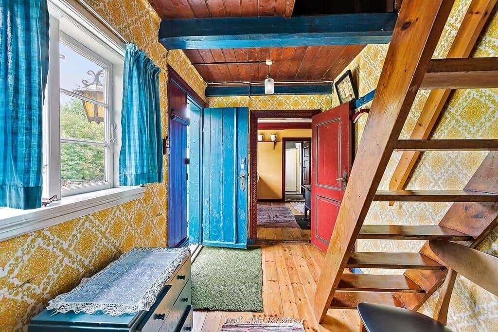Haus mit Holztreppe, blauer Tür und gelbem Tapetenmuster an den Wänden.