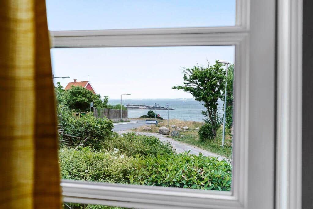 Durch das Fenster blickt man auf eine Straße, Grünflächen und das Meer.