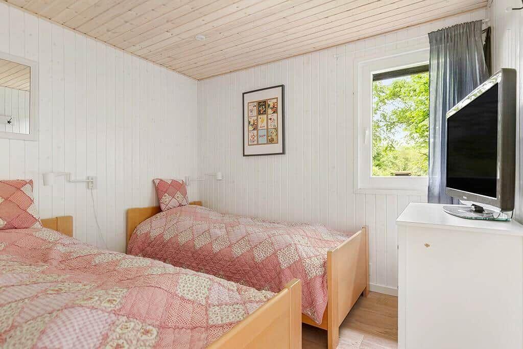 Zwei Betten mit rosa Quilt, Fernseher und Fenster mit Blick auf Grün.