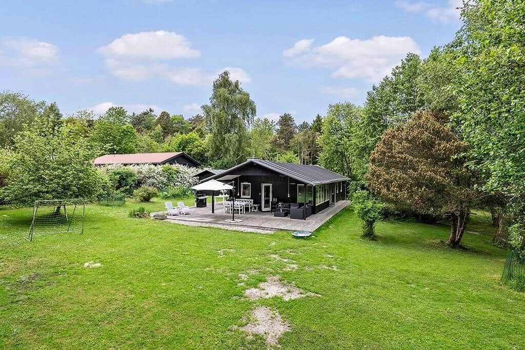 Schwarze Hütte mit Terrasse, Garten und Grillplatz im Grünen.