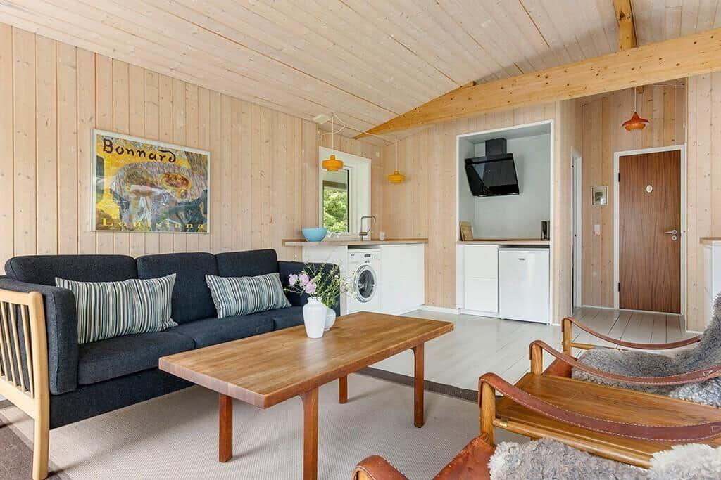 Wohnzimmer mit Sofa, Tisch und Küchenbereich. Holzwände und Decke.