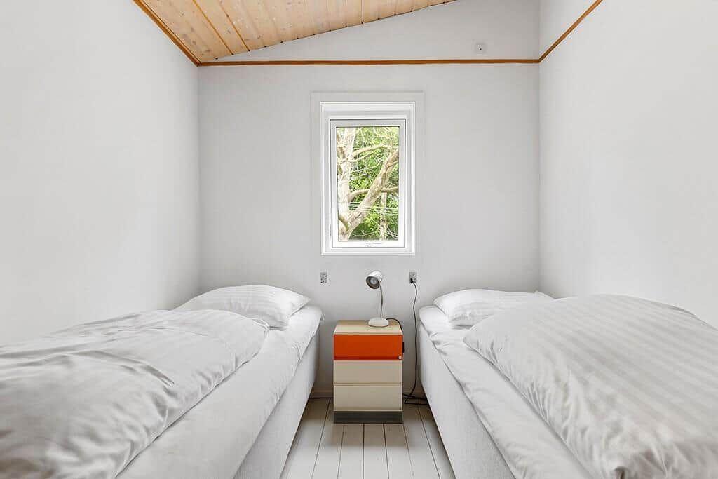 Zwei Betten mit weißen Bettwäschen, ein Fenster und ein Nachttisch mit Lampe.