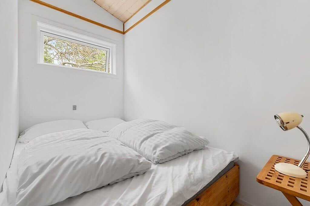 Ein Bett mit weißen Laken, einem Holzgestell und einem kleinen Nachttisch mit Lampe.