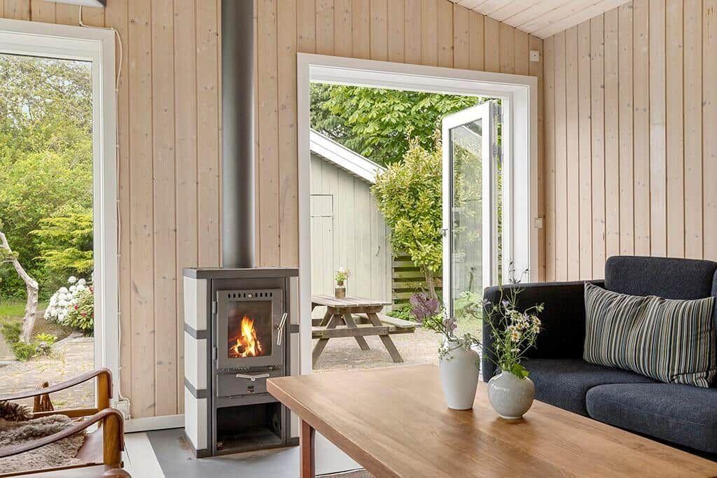 Wohnraum mit Kamin, Sofa und Tisch. Durchgänge zu Garten und Terrasse.