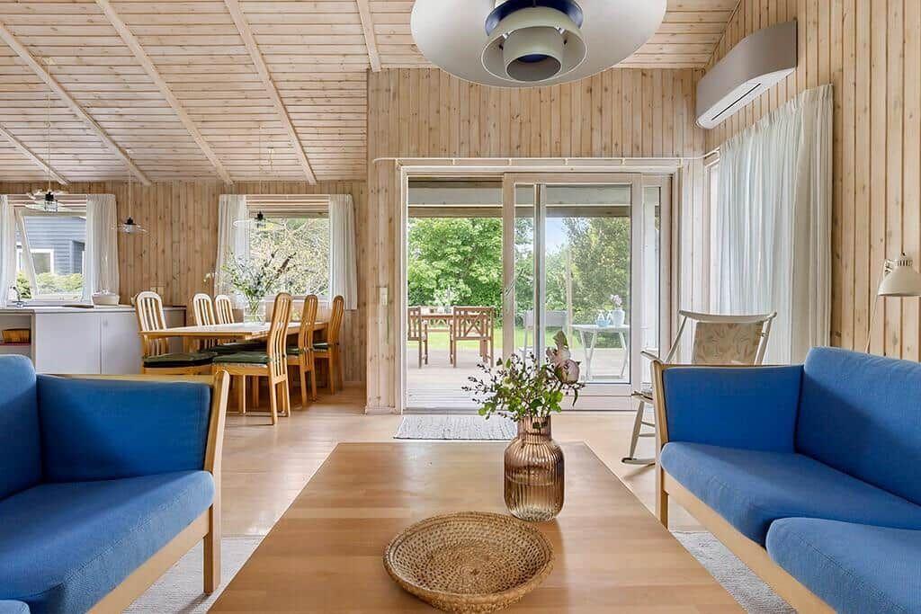 Wohnzimmer mit blauen Sitzgelegenheiten, Holztisch und Blick auf den Garten.