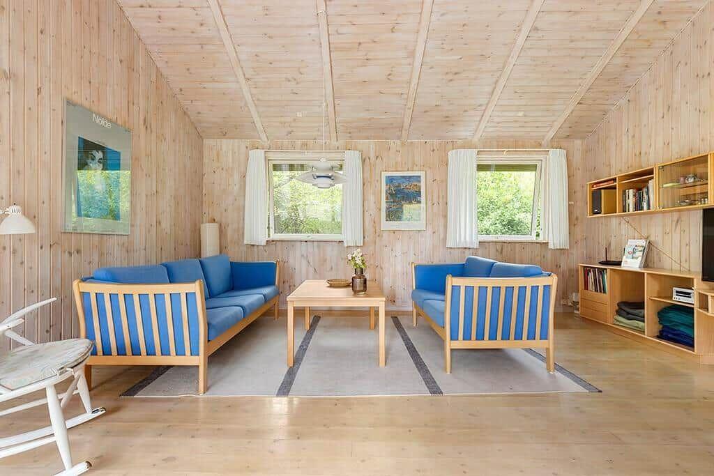 Wohnzimmer mit Holzwand, blauen Sesseln und Fenstern zum Garten