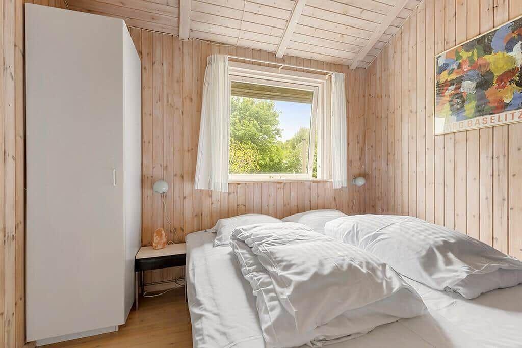 Schlafzimmer mit Holzwand, Bett, Fenster und Kleiderschrank.