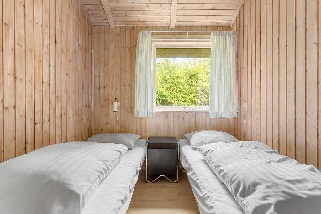 Zwei Betten in einem Holzhauszimmer mit Fenster und Nachttisch.