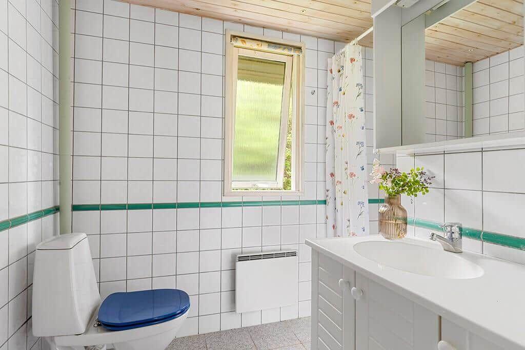 Badezimmer mit Toilette, Waschbecken und Fenster. Wandfliesen und Holzdecke.