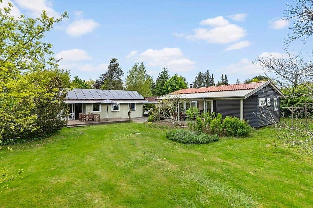 Zwei Häuser mit Terrassen und Garten unter blauem Himmel.