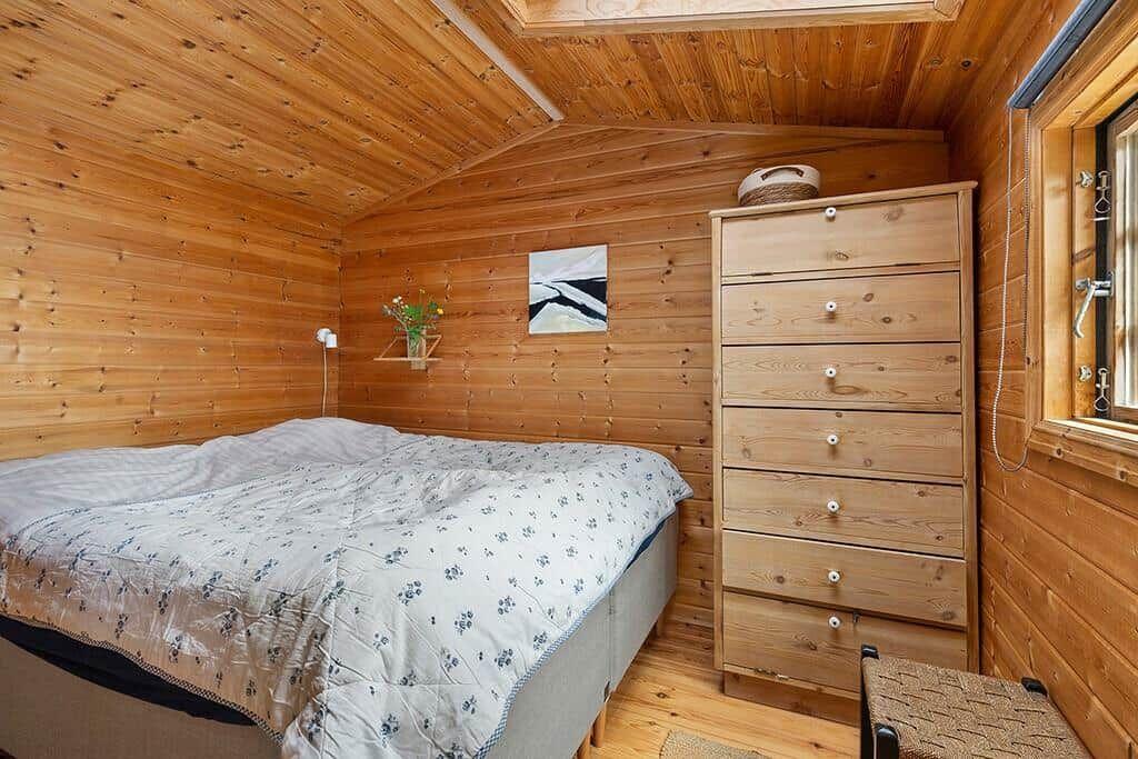 Schlafzimmer mit Holzwand, Bett, Schrank und Fenster.