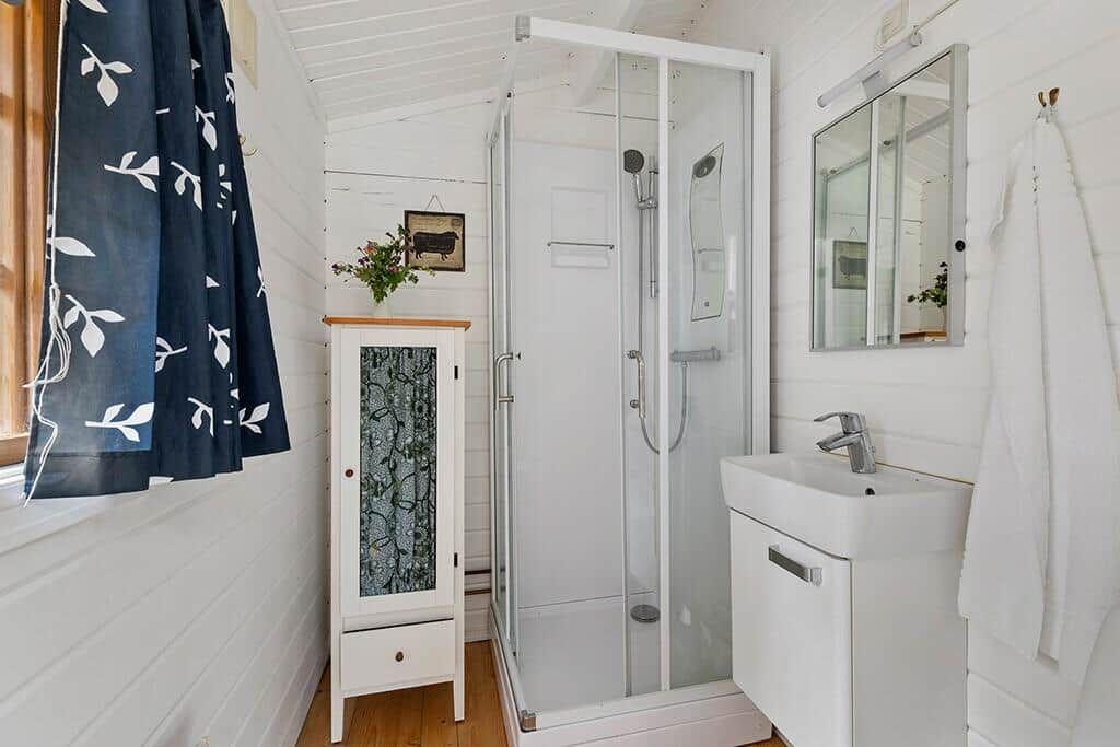Dusche, Waschbecken und Kleiderschrank in einem hellen Badezimmer mit Holzboden und blauem Vorhang.