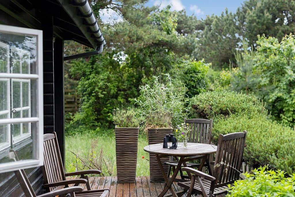Terrasse mit Tisch und Stühlen, umgeben von grüner Vegetation und einem Fenster.