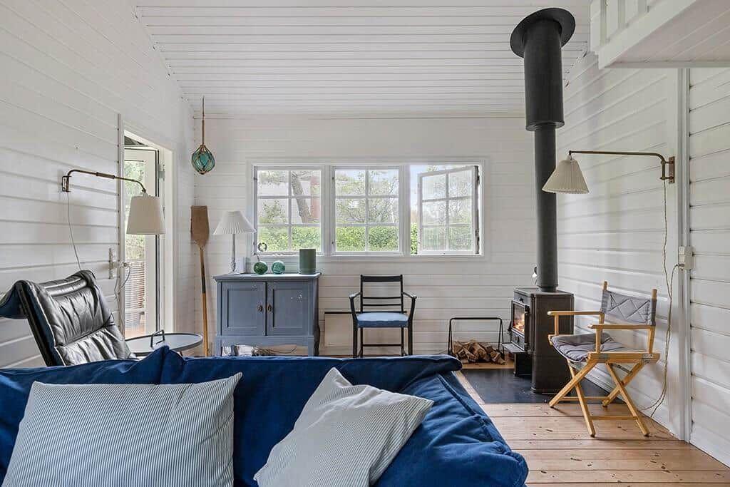 Ein Raum mit blauem Sofa, Holzfußboden und Kaminofen. Fenster, Stühle und Schrank sind sichtbar.