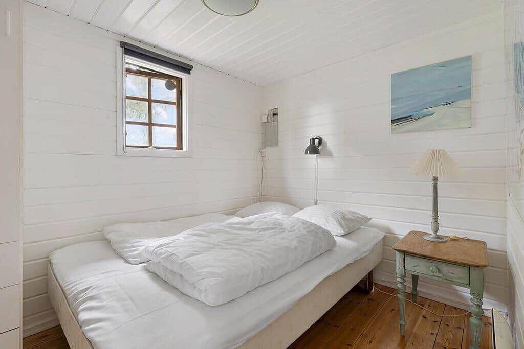 Schlafzimmer mit weißem Bett, Holzboden und Fenster mit Blick nach draußen.