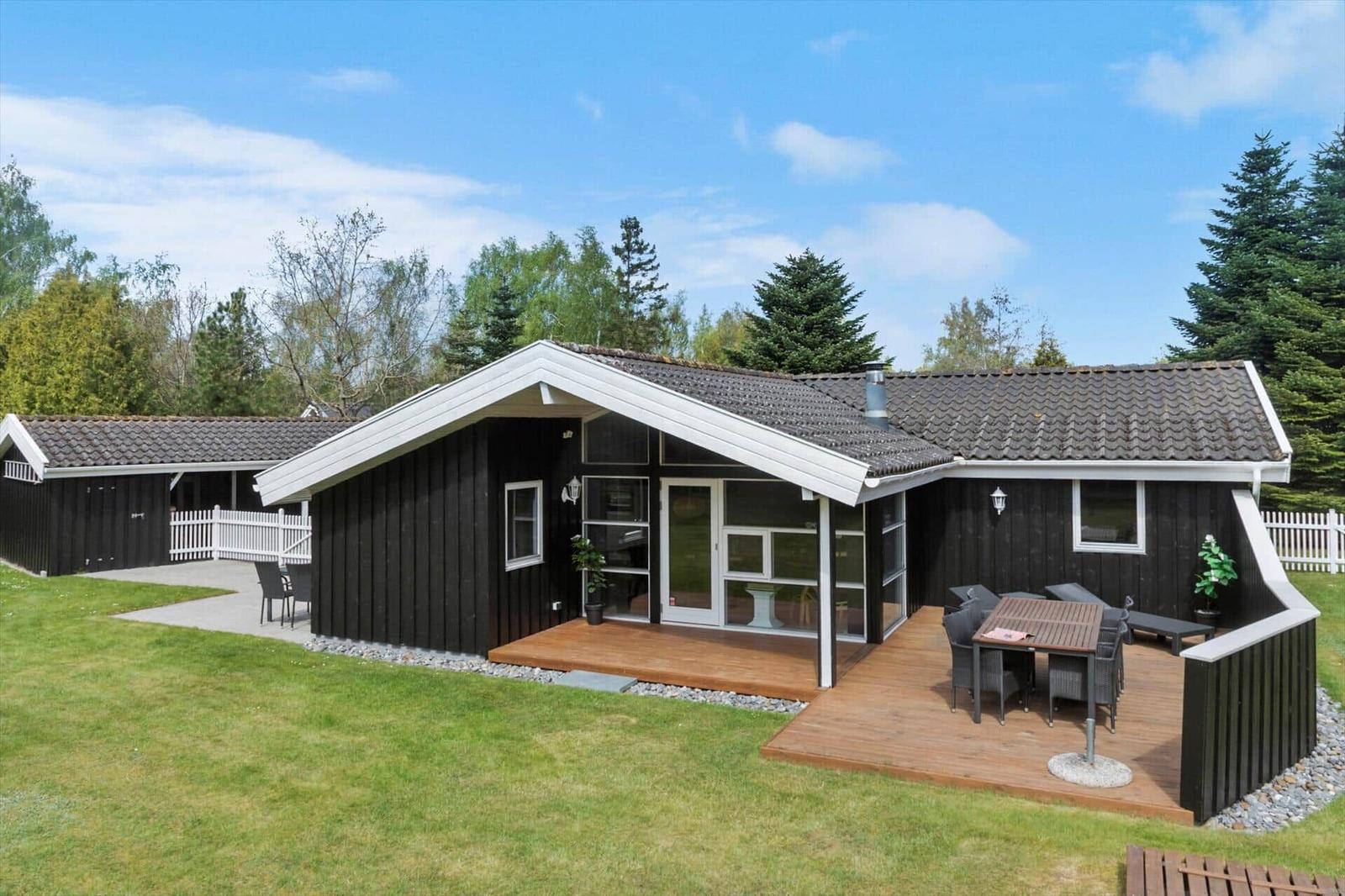 Moderne Holzhütte mit Terrasse, Garten und Grillbereich. Gepflegte Umgebung mit Bäumen.