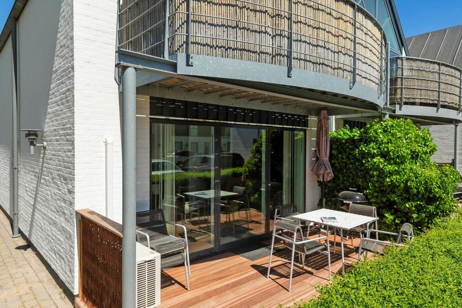 Terrasse mit Tisch, Stühlen und Grill. Glasfront und Balkon mit Bambusverkleidung.