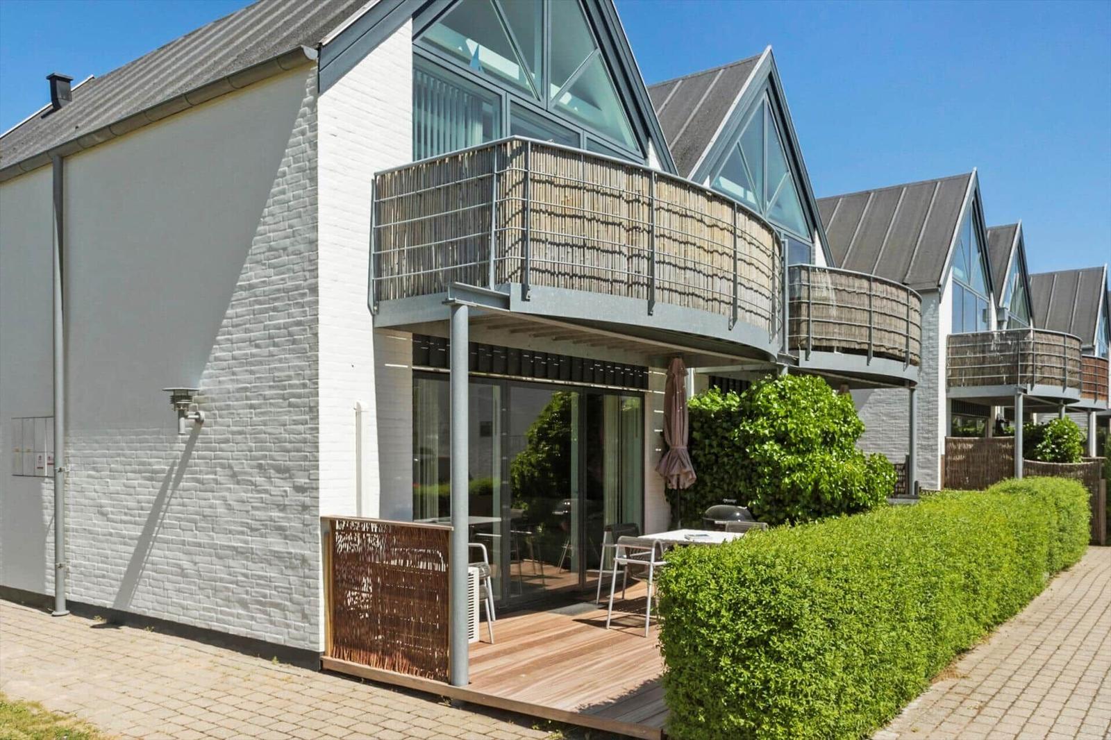 Moderne Ferienwohnung mit Balkon, Terrasse und Grillplatz. Weiße Fassade und grüne Hecke.
