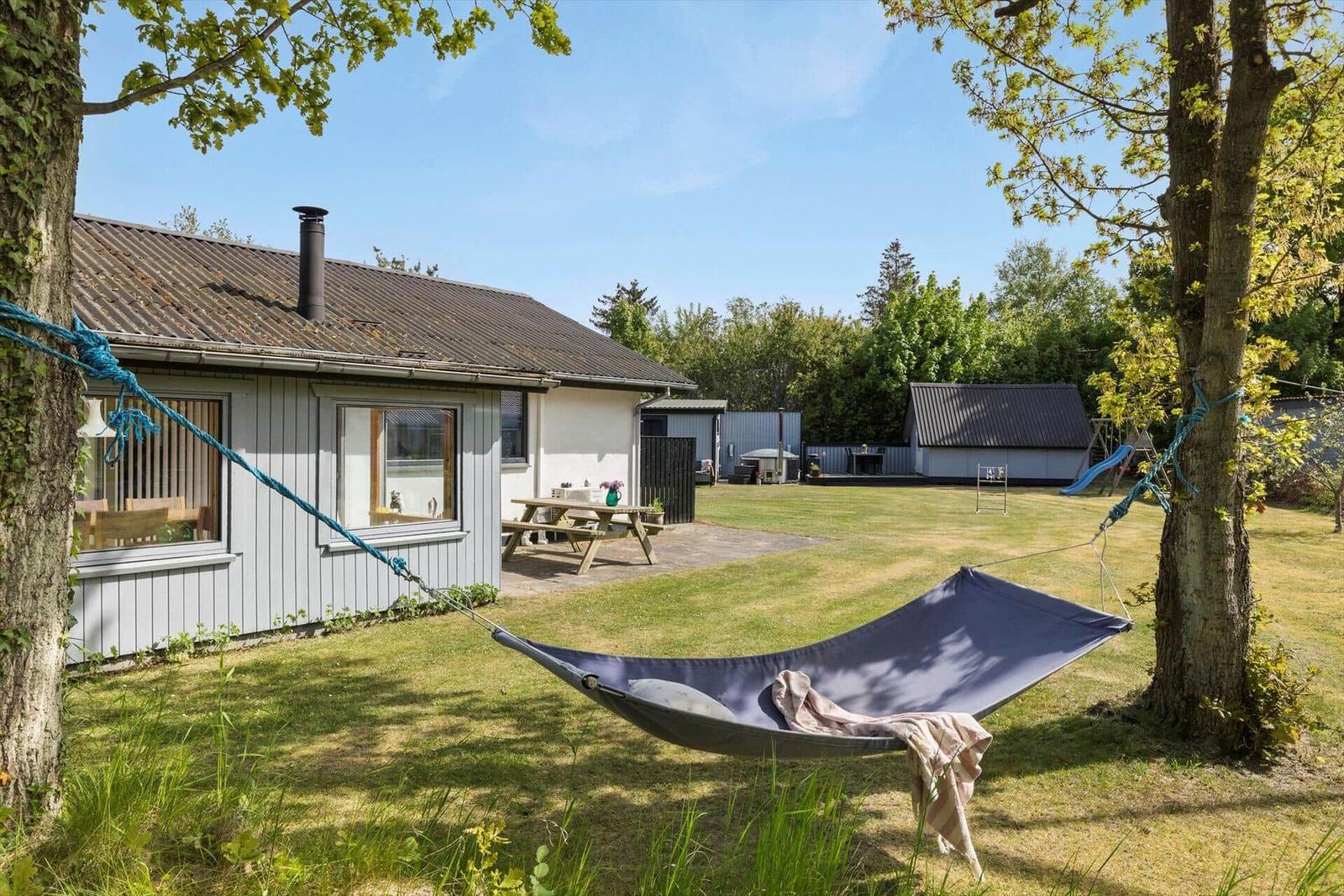 Garten mit Tisch, Stuhl und Hühnern. Vogelhaus und Sträucher im Hintergrund.