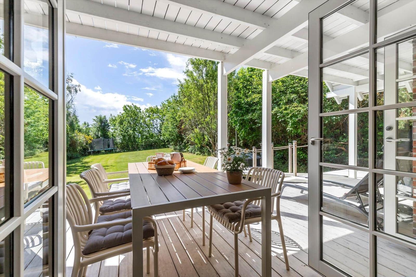 Terrasse mit Tisch und Stühlen, Blick auf grünen Garten und Himmel.