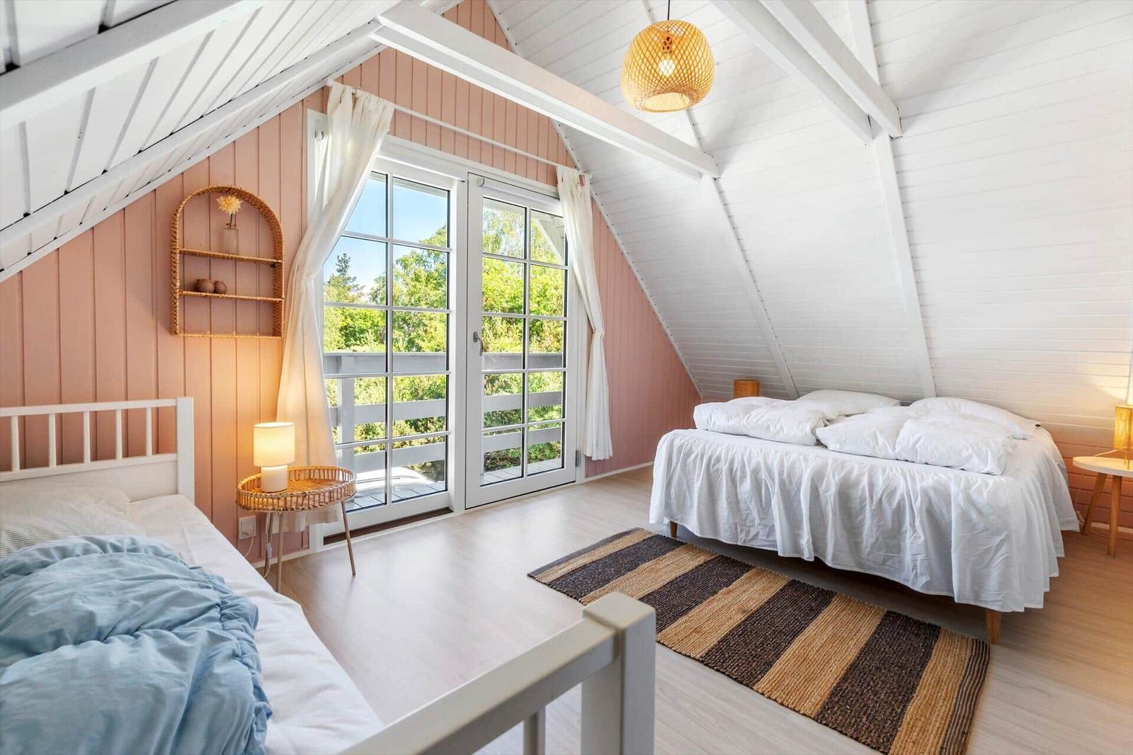 Zwei Betten mit weißen Laken, Terrassentür, Holzboden und rosa Wandverkleidung.
