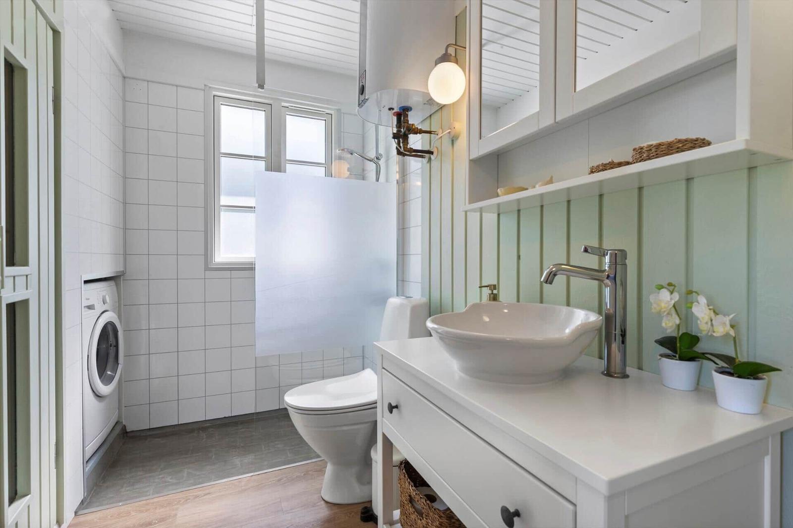 Badezimmer mit Waschmaschine, Toilette und Waschtisch mit Spiegel.
