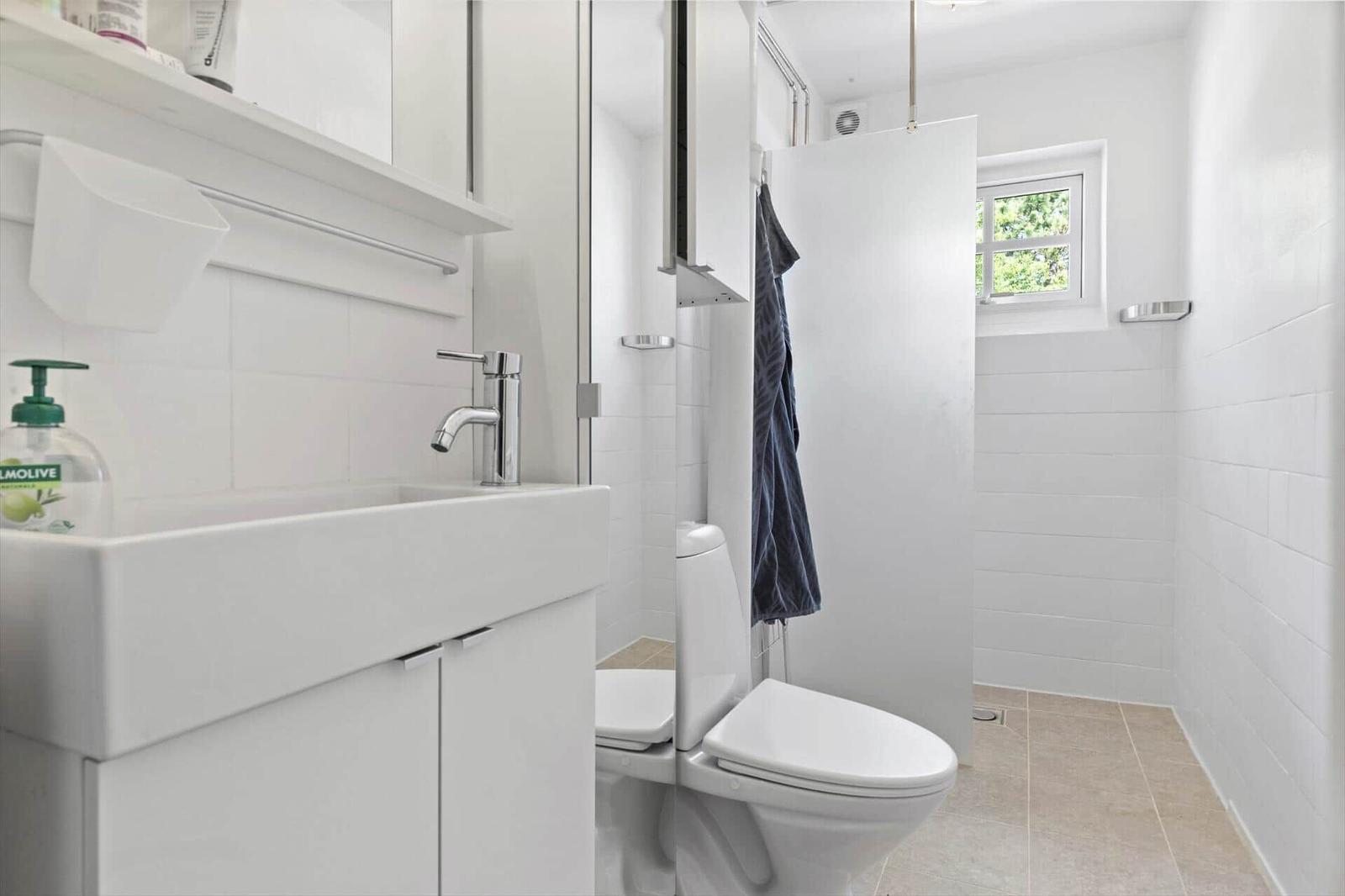 Badezimmer mit Waschbecken, Toilette und Dusche. Fenster mit Blick auf Grün.