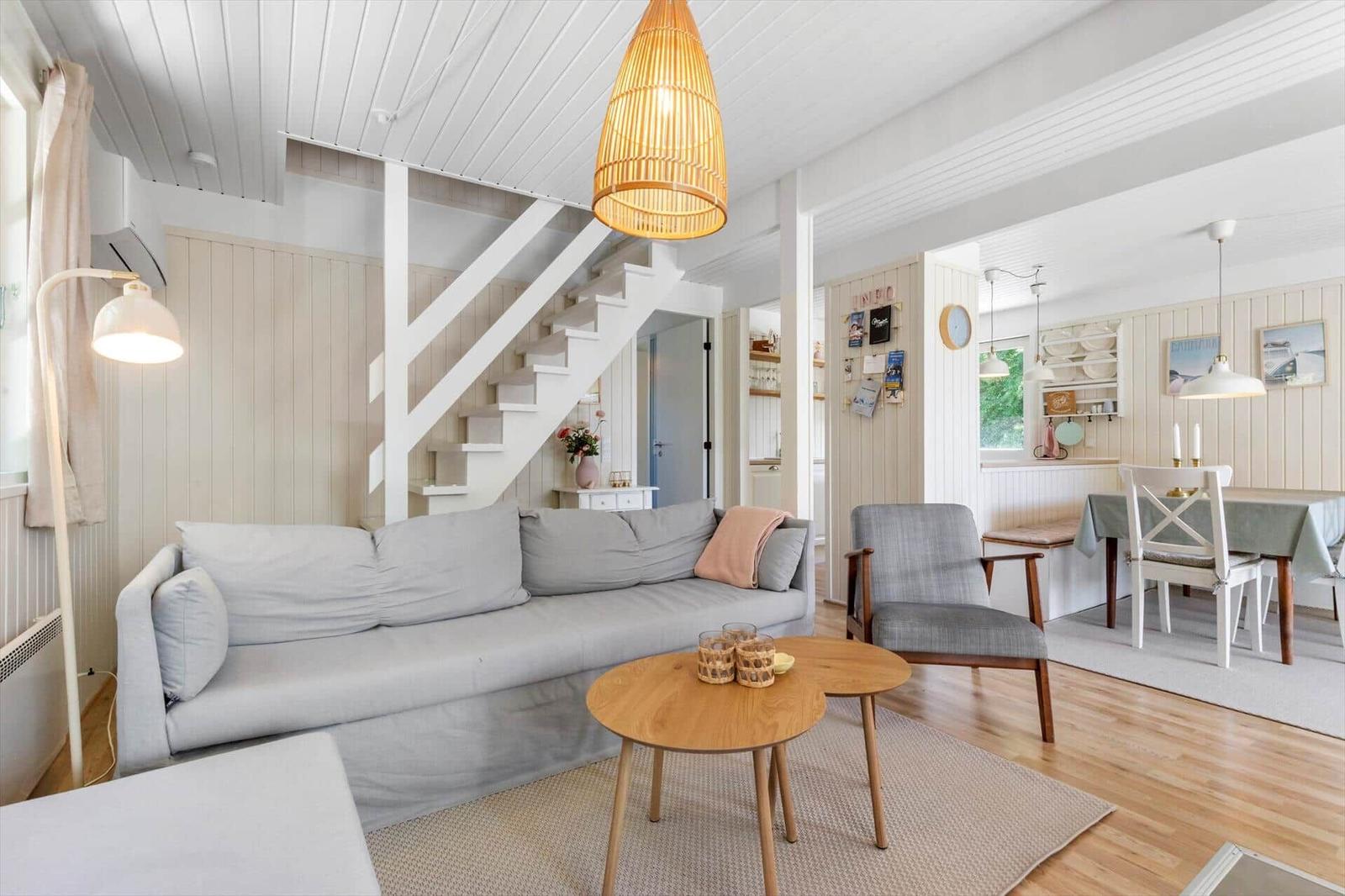 Wohnzimmer mit Sofa, Tisch und Stuhl. Treppenhaus führt nach oben. Essbereich mit Tisch und Stühlen.