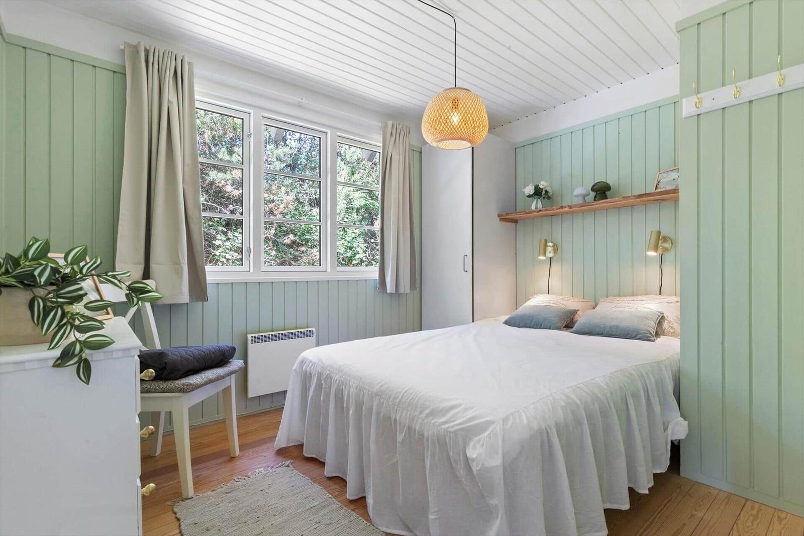 Schlafzimmer mit Bett, Fenster und grünen Wänden. Hängelampe und Schrank sind sichtbar.