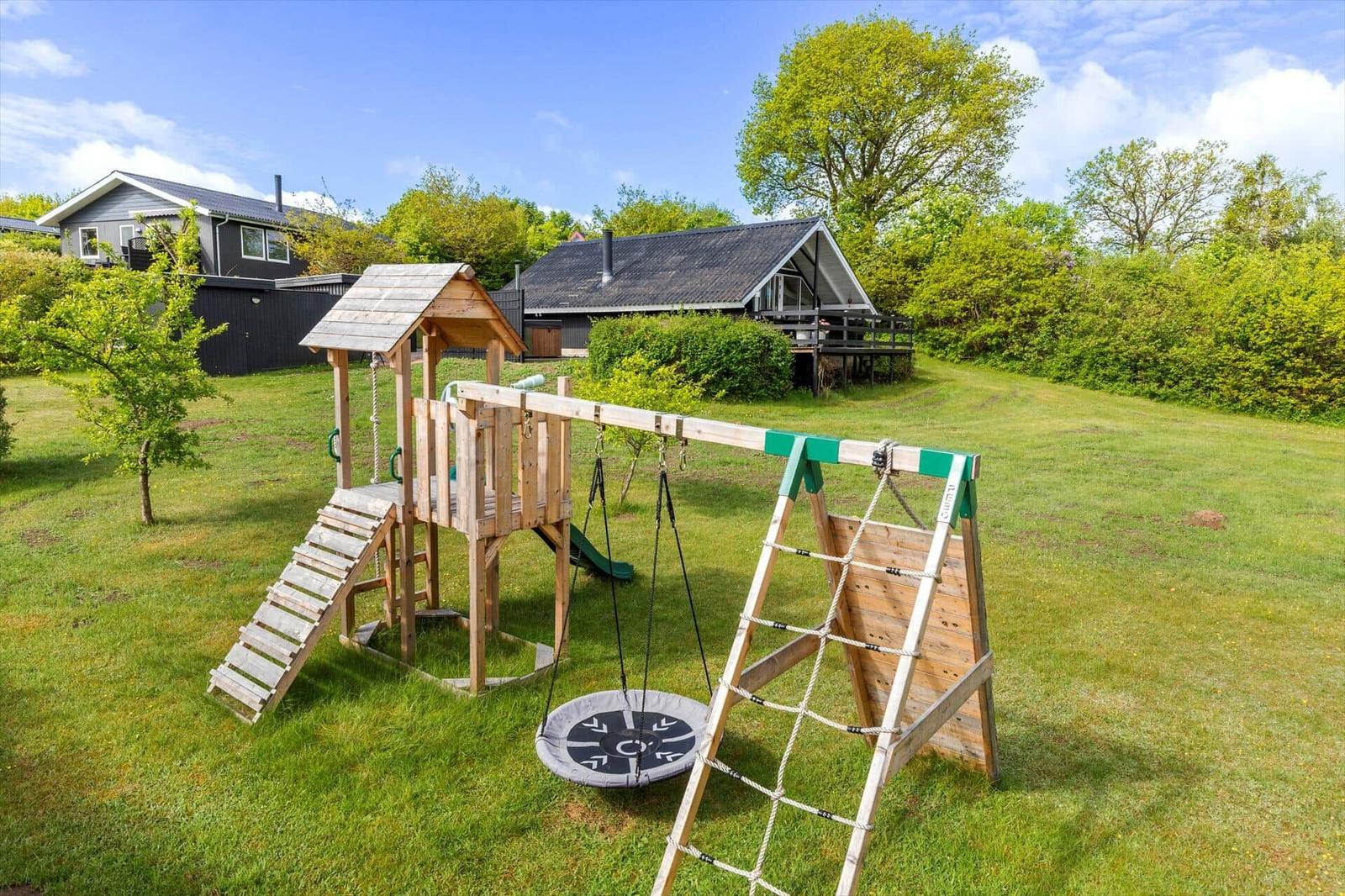 Holzspielplatz mit Rutsche, Schaukel und Klettergerüst auf grünem Rasen.
