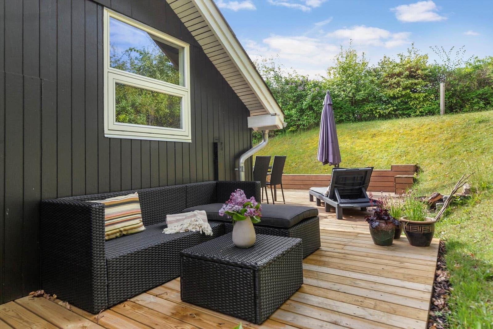 Terrasse mit Sitzgruppe, Liegestuhl und Sonnenschirm neben einem Haus mit dunkler Fassade.