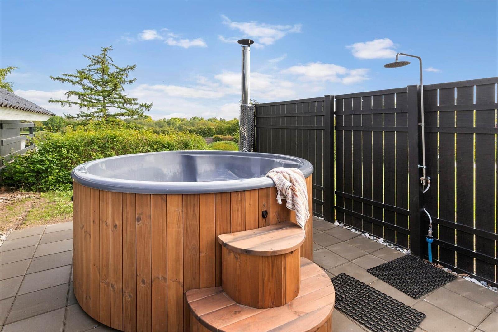 Hochwertige Holz-Hot-Tub mit Außendusche und Blick auf grüne Landschaft.