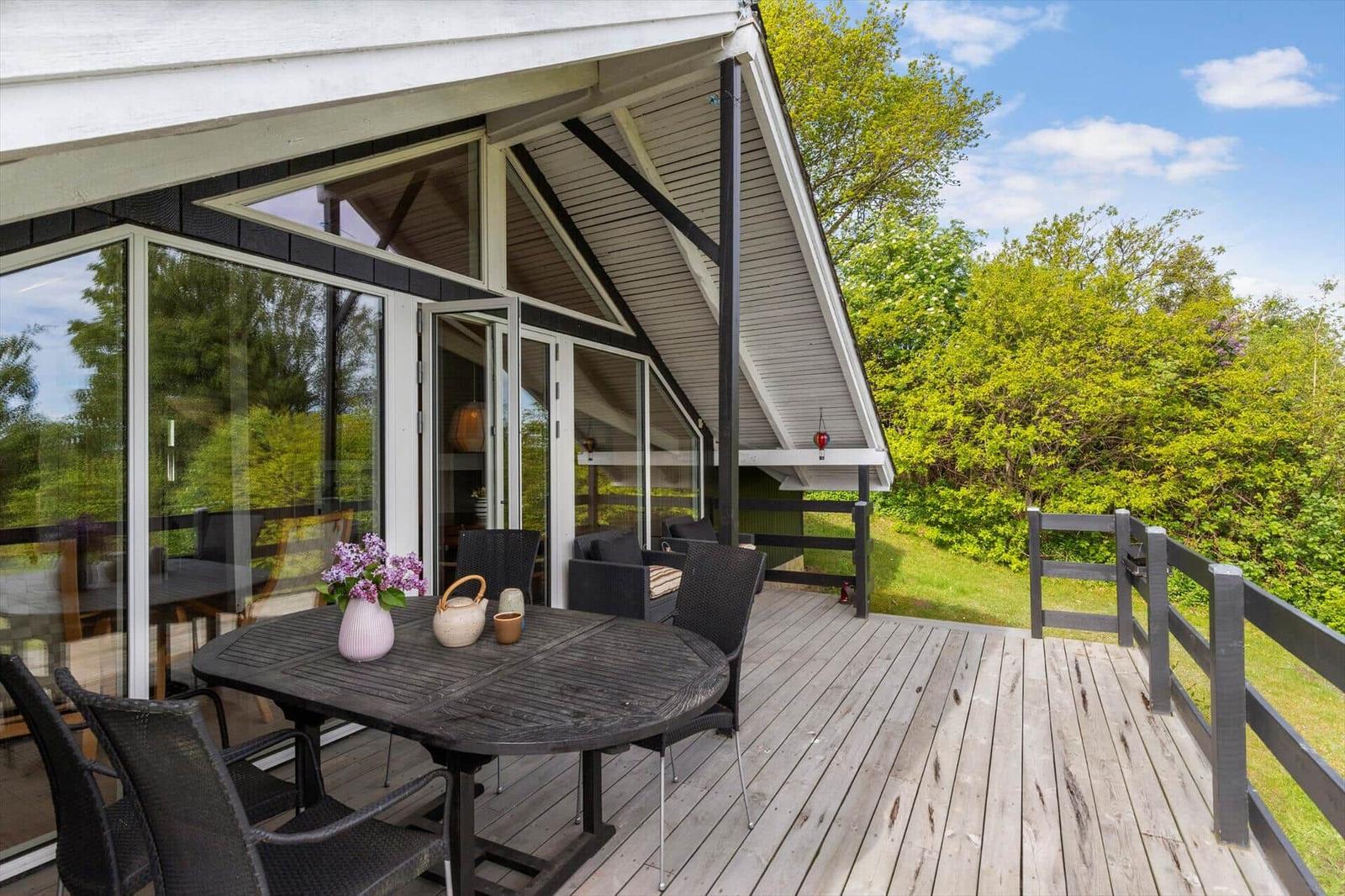 Terrasse mit Tisch und Stühlen, Blick in Wohnbereich, umgeben von grüner Vegetation.