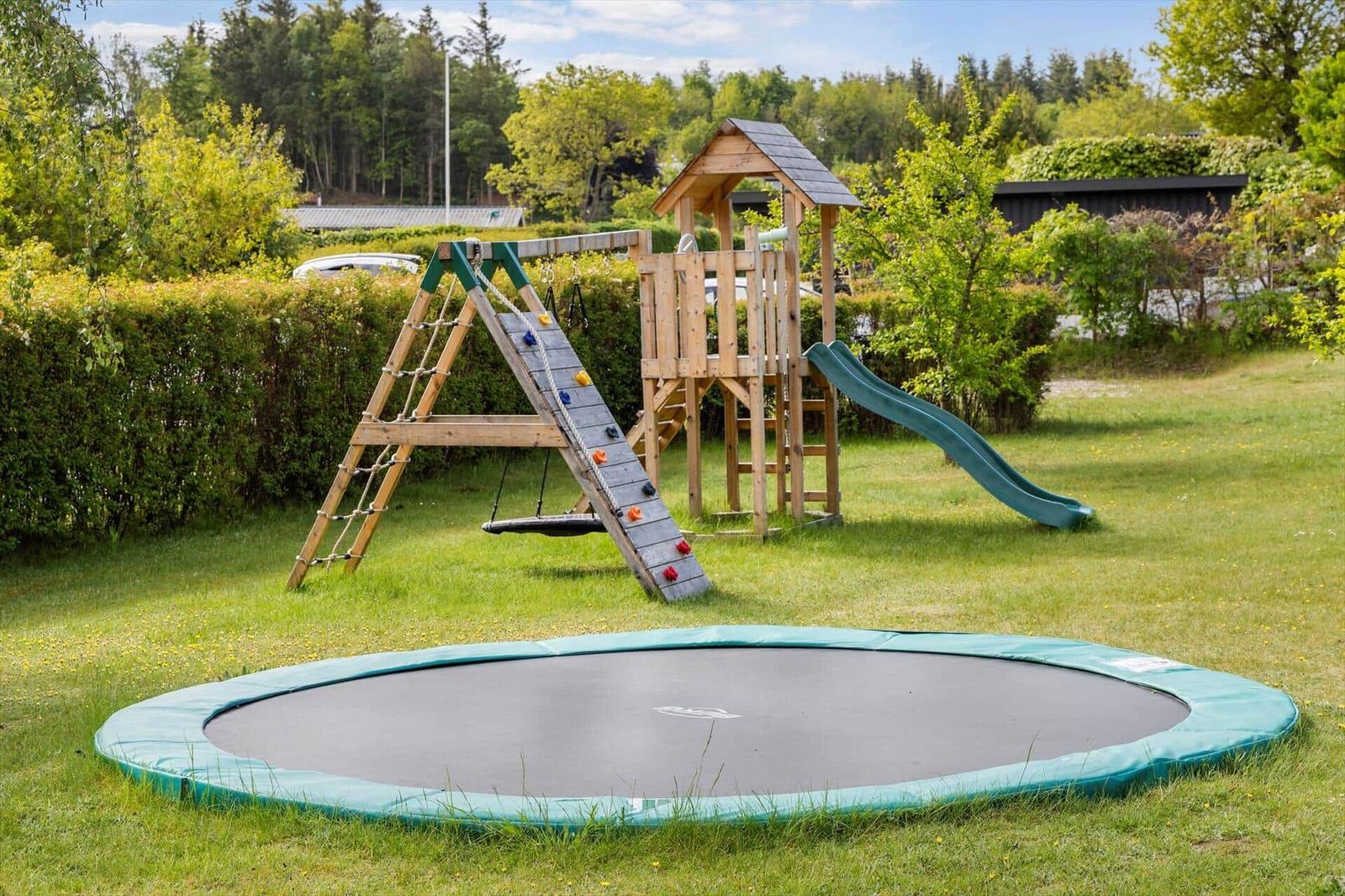 Großer Garten mit Trampolin und Holzspielplatz mit Rutsche und Kletterwand.