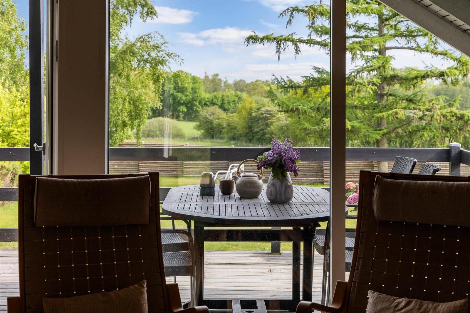 Terrasse mit Tisch und Stühlen, Blick auf grüne Landschaft und Bäume.