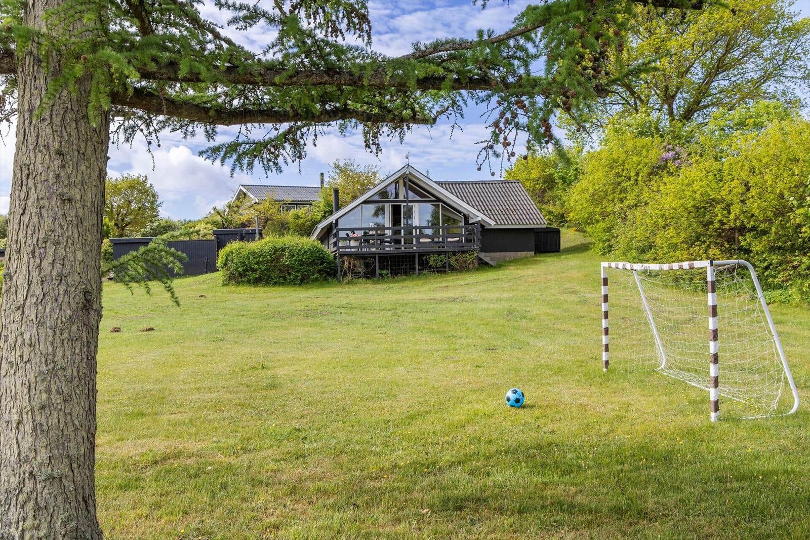 Haus mit Terrasse, Fußballtor und Ball auf grünem Rasen unter Bäumen.