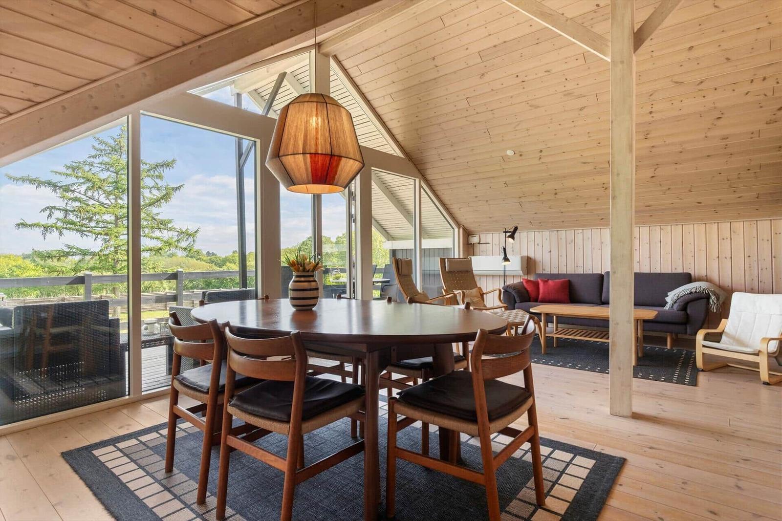 Essbereich mit Tisch und Stühlen, Sitzbereich mit Sofa und Couchtisch, Holzdecke und große Fenster.