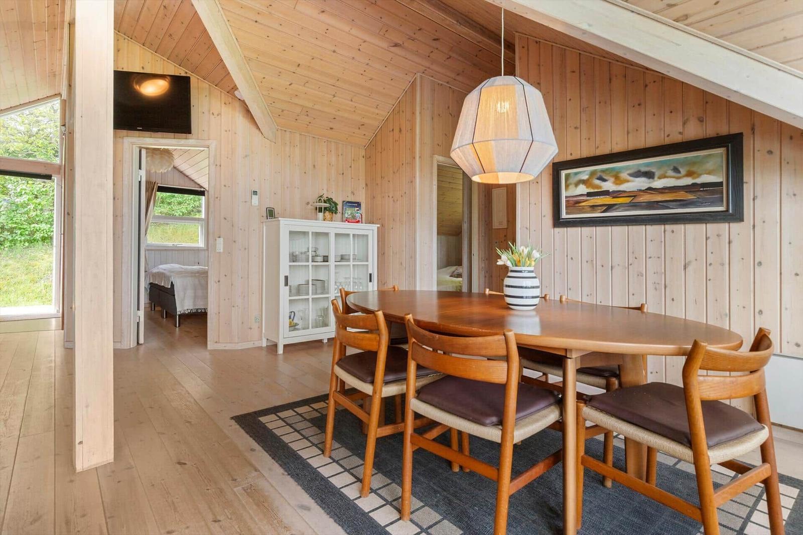 Esszimmer mit Holztisch, Stühlen und Wandbild. Holzwände und -boden. Fernseher und Schrank im Hintergrund.