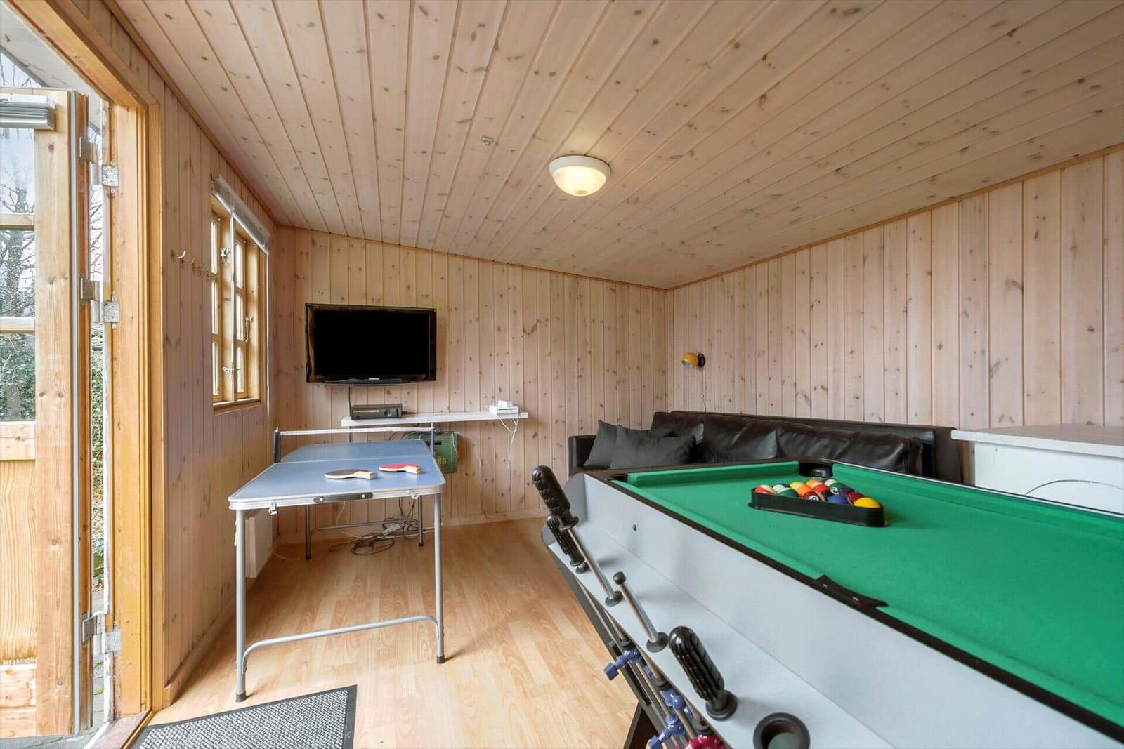 Room with ping pong table, dart and pool table. Wooden walls and ceiling. Black sofa.