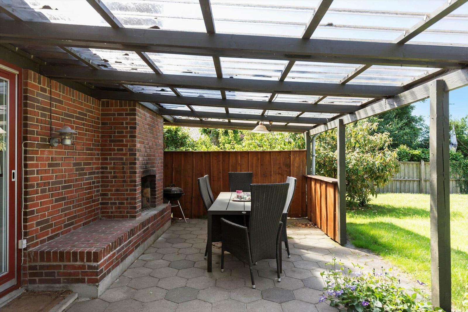 Red garden house with hot tub and umbrella on paved yard.