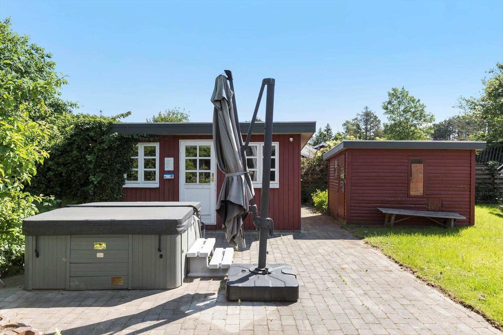 Red wooden shed with white windows and door. Garden with hot tub and umbrella.