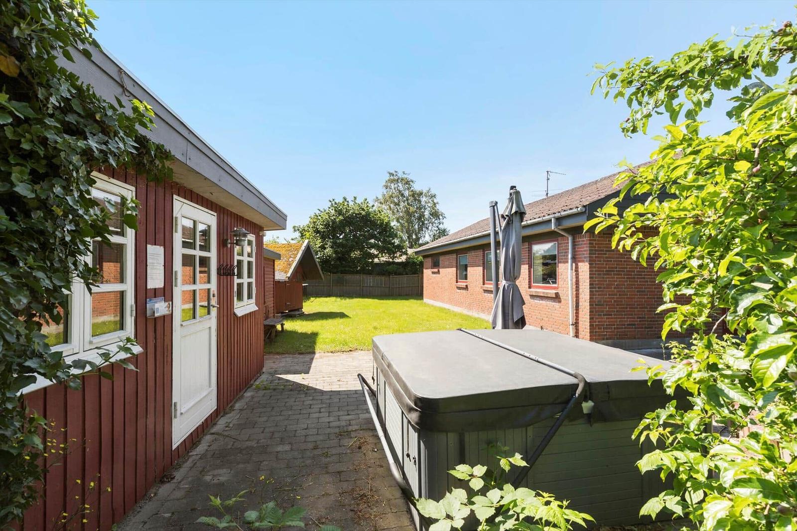Backyard with swing under pergola, green lawn and brick house in background.