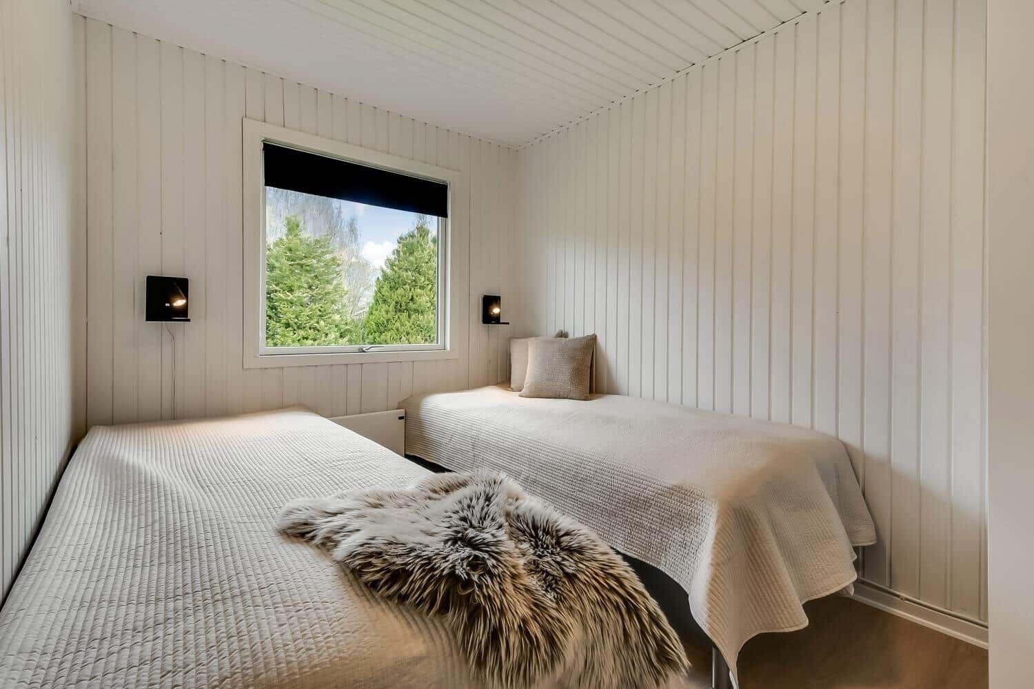 Ein dunkelgraues Ferienhaus mit weißem Fensterrahmen und Eingangstür. Grasfläche und Bäume im Hintergrund.