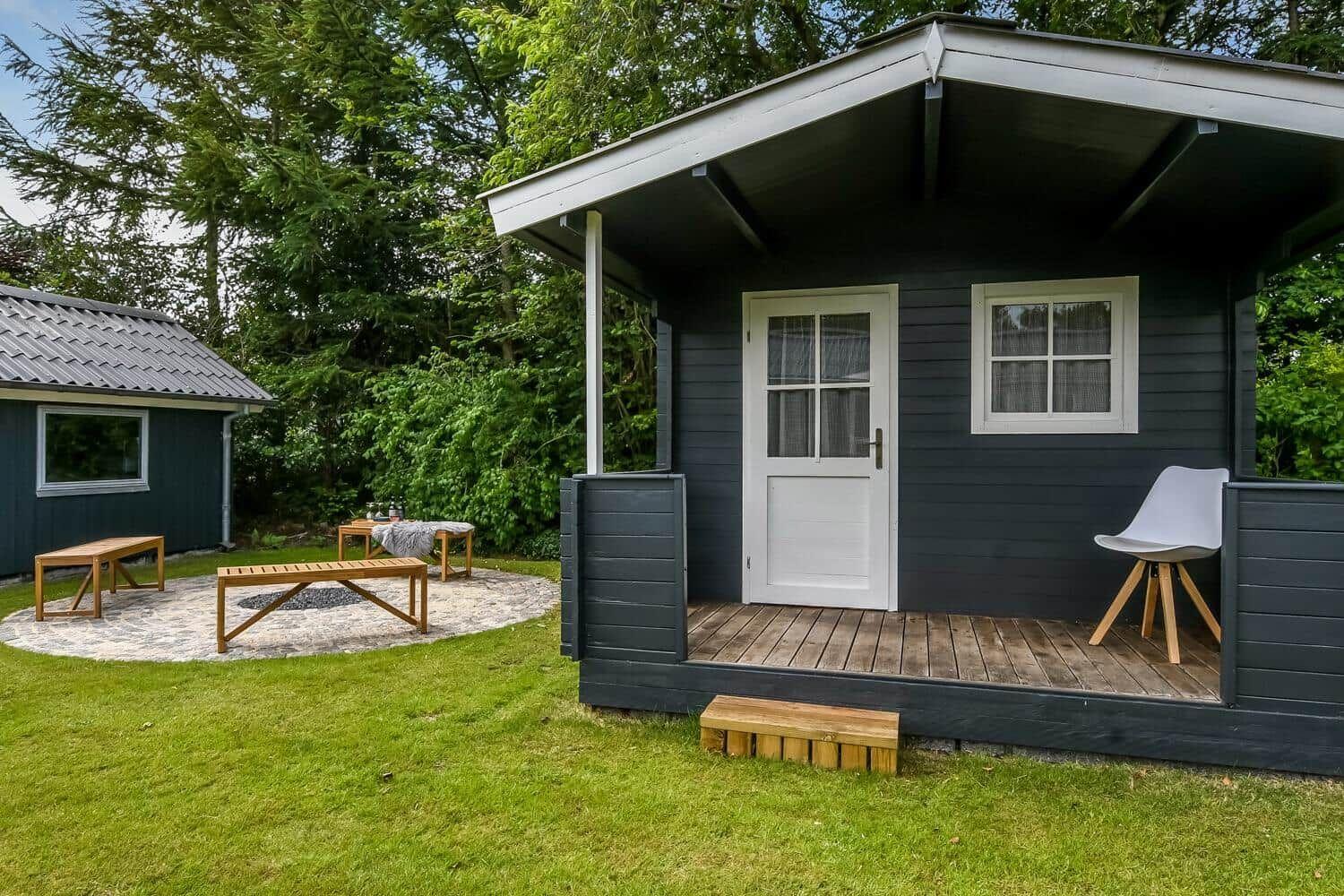 Moderne Holzhütte mit Terrasse, Liege und Sitzgelegenheit im Garten.