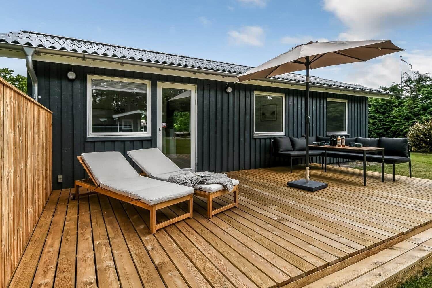 Terrasse mit Sonnenschirm, Liegestuhl und Sitzgruppe vor einem Haus mit dunkler Fassade.
