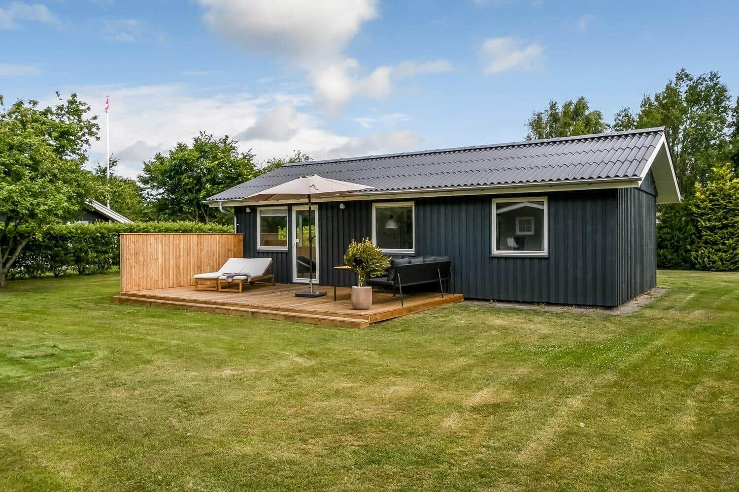 Hintergrund zeigt eine Holterrasse mit zwei weißen Sesseln vor einem grauen Haus.