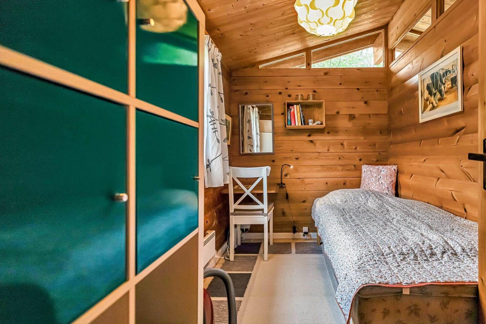 Schlafzimmer mit Holzwänden, Bett und Fenster.
